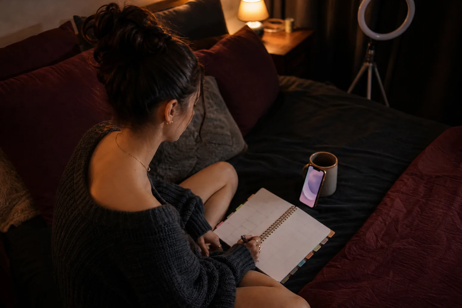 Creator on her bed at night filling in a paper weekly planner next to her phone